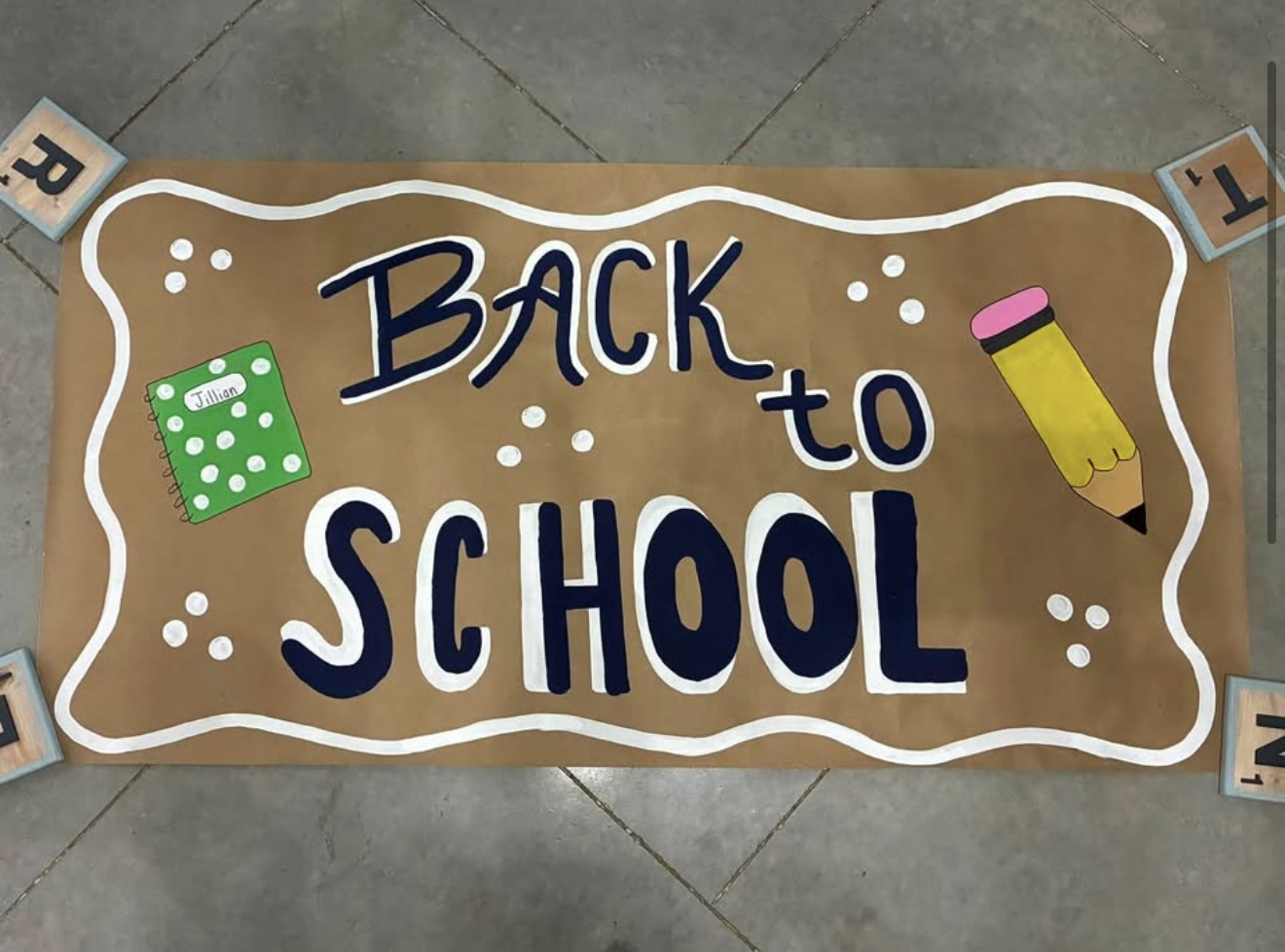 Hand-painted kraft paper 'Back to School' banner in navy lettering with a green notebook and yellow pencil illustration